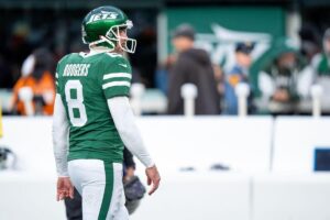 New York Jets quarterback Aaron Rodgers looking away from the football field.