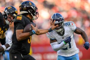 Washington Commanders quarterback Jayden Daniels stiff-arms a defender.