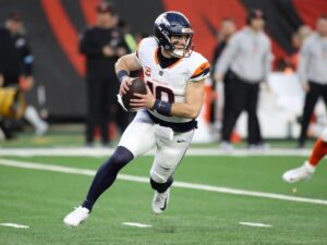 Denver Broncos quarterback Bo Nix scrambling with a football.