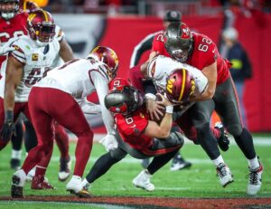 Tampa Bay Buccaneers quarterback Baker Mayfield is tackled down by Washington Commanders defenders.